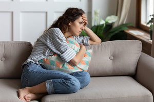 Stressed woman sitting on couch with head in hand
