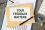 A notebook, note card and pen. The note card reads "Your feedback matters"