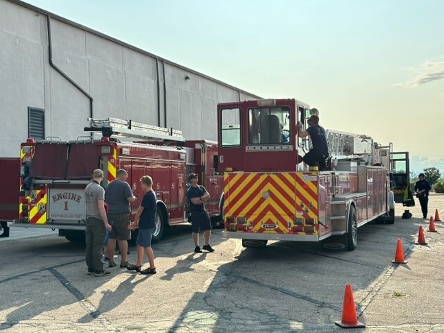 three fire engines with kids looking around them with fire fighters