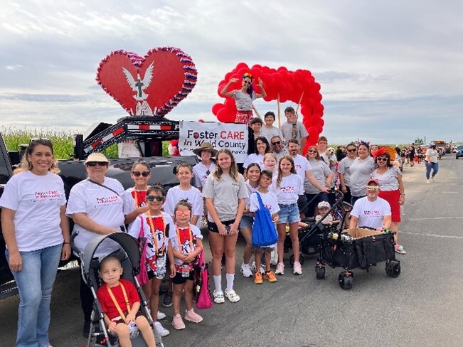 Foster Care in Weld County float with large red heart, with adults and kids posing in front, during Milliken's Beef and Bean Parade