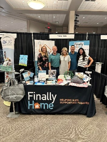 "Finally Home" workers posing at a booth with handouts and brochures.