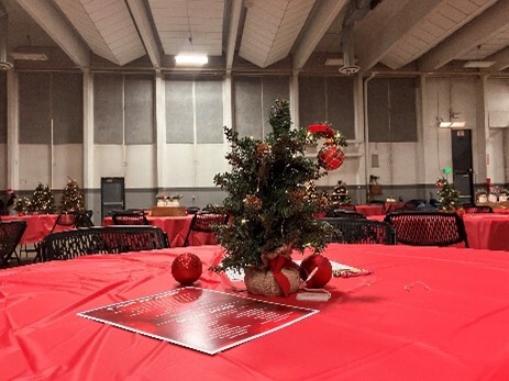 A centerpiece, a small Christmas tree with red ornaments, sitting on a table covered in a festive red tablecloth