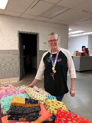 A volunteer smiling and posing beside a table covered in wrapped Christmas presents