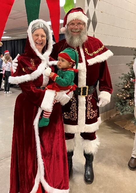A man and woman dressed as Santa and Mrs. Claus, holding a baby dressed as an elf
