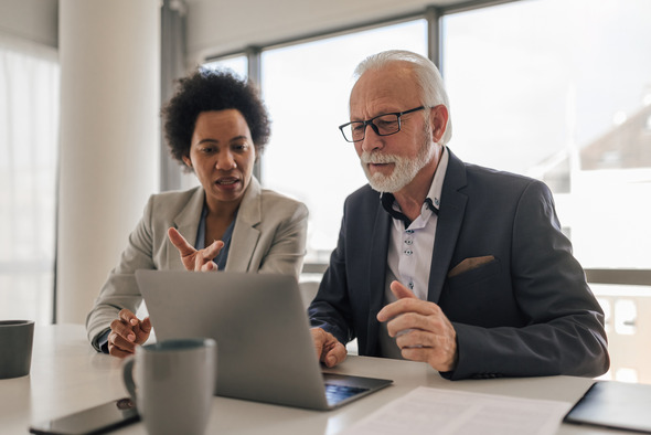 An older man on a laptop, getting some instruction from a woman sitting beside him