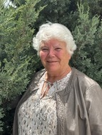 A photo of Mary Collard, 2024 Hall of Fame Recipient, smiling beside an evergreen tree