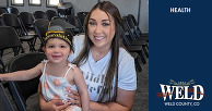 A smiling mother holds her child, who is wearing a graduation cap, at the NPF graduation event.