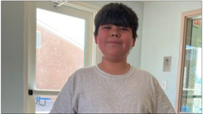 A young boy, Oscar, smiling and standing in a room next to a window.
