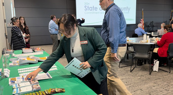 A woman grabbing items of of a table at the State of the County event.