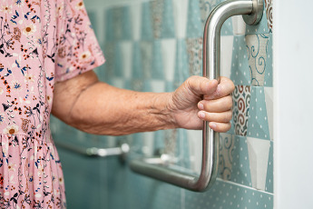 Senior woman holding onto a grab bar for support in a bathroom