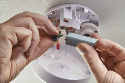 A person changing batteries in a smoke detector.
