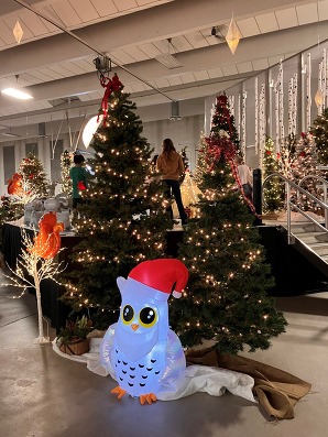 An inflatable white owl in a Santa hat in front of lit Christmas trees