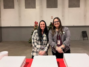 Two female Weld County employees with gloves ready to serve pizza