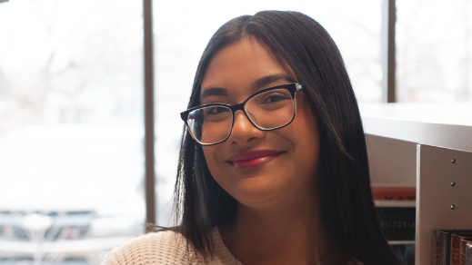 A teenage girl with black hair and black framed glasses smiling at the camera.