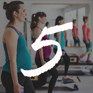 Pregnant women in brightly colored tank tops doing prenatal pilates in a room at the gym.