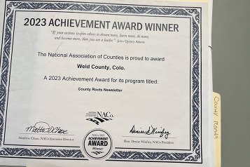 A 2023 Achievement Award recognizing the County Roots newsletter. The award is up against a County Roots work folder.