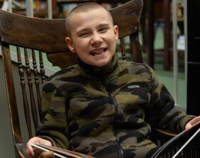 James, a preteen boy, sitting in a wooden chair and smiling