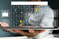 Person holding a laptop with a monthly calendar on the screen.