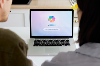 The backs of two people sitting on either side of a laptop. The laptop screen says Microsoft Co-Pilot.