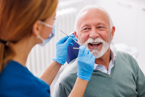 Older man sitting in a chair while a dentist examines his teeth