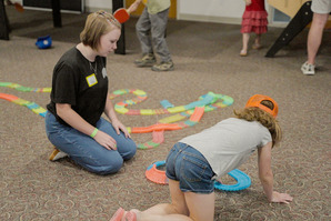 A young girl and adult volunteer playing with a train tracks toy.