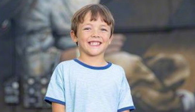 A young boy with light brown hair and a big smile.