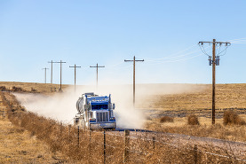 A heavy truck stirring up dust on a dirt road.