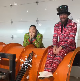 Public Works staff dressed in Christmas suits sitting on a snow plow blade