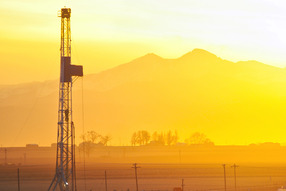 Oil and gas drilling rig in Colorado with the sun setting over the mountains.