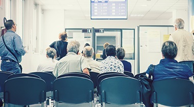 People in a waiting room looing at a monitor.