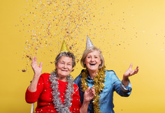 Two older women in party hats throwing confetti