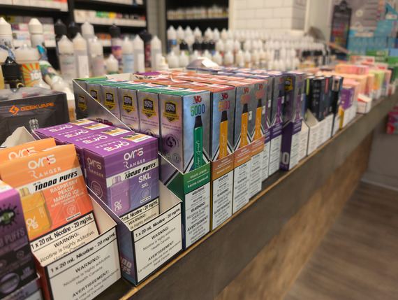 Multiple vape devices and flavored nicotine products in a store showcase.