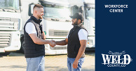 Business owner and apprentice shaking hands in front of fleet vehicles