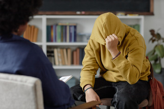 Boy covering face with hoodie while talking to case manager