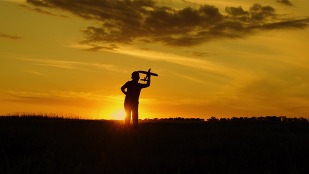 Silhouette of a young boy playing with a toy airplane at sunset