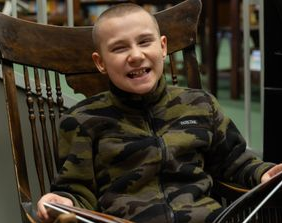 A young boy with a shaved head is smiling widely