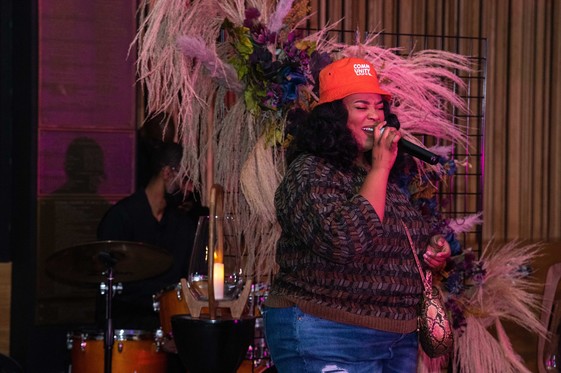 Woman sings into a mic in front of a drummer