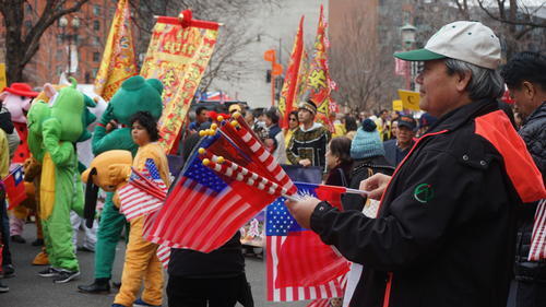 A man passes out American flags to passers-by, looking out at the parade line-up
