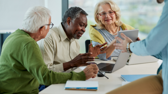 Three seniors sit at a table with a computer