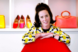 Kate Spade smiles at the camera and rests her arms over a red chair