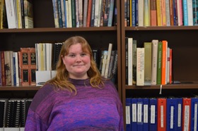 Photo of a young woman standing in front of shelves of books