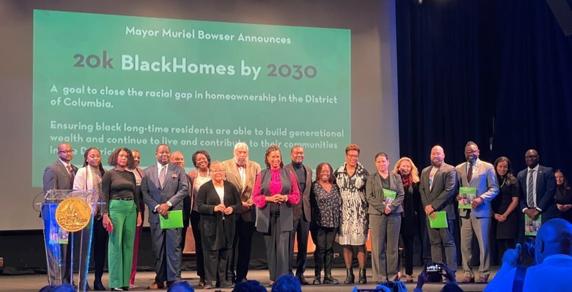 The Black Homeownership Strike Force participants smile in a row on stage at the project kick-off