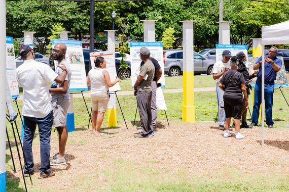 Residents gather around poster boards on easels to review plans from OP in a grassy outdoor setting