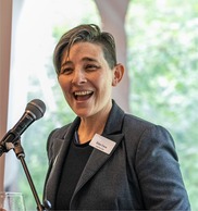 Image of a white woman (Eliza Cava) speaking into a microphone