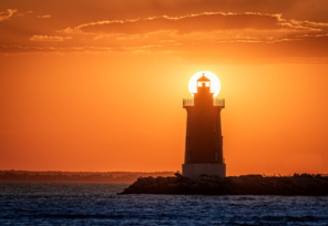 Lighthouse at sunset with the sun aligned behind its light.          Ask ChatGPT