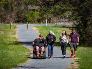 Four people, including one using a Trackchair, traversing together on a paved park trail.