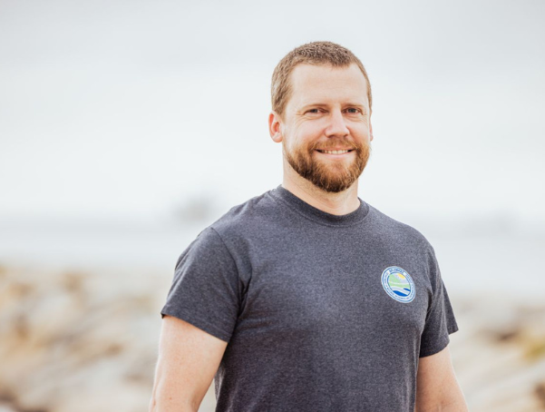 Jesse Hayden smiling on the beach wearing a DNREC t-shirt.