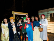 A group of people dressed in colorful costumes, including fairy-tale and video game characters, pose together outdoors at night.