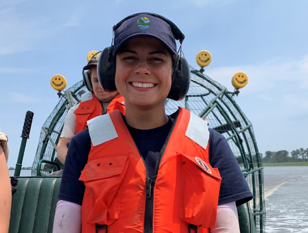 DNREC employee Olivia Allread smiling on a boat with headphones as she is working in the field. 
