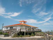 visitors enjoy the view from the DuPont Nature Center deck overlooking the beach. the building behind them with a beautiful clear sky as the backdrop.